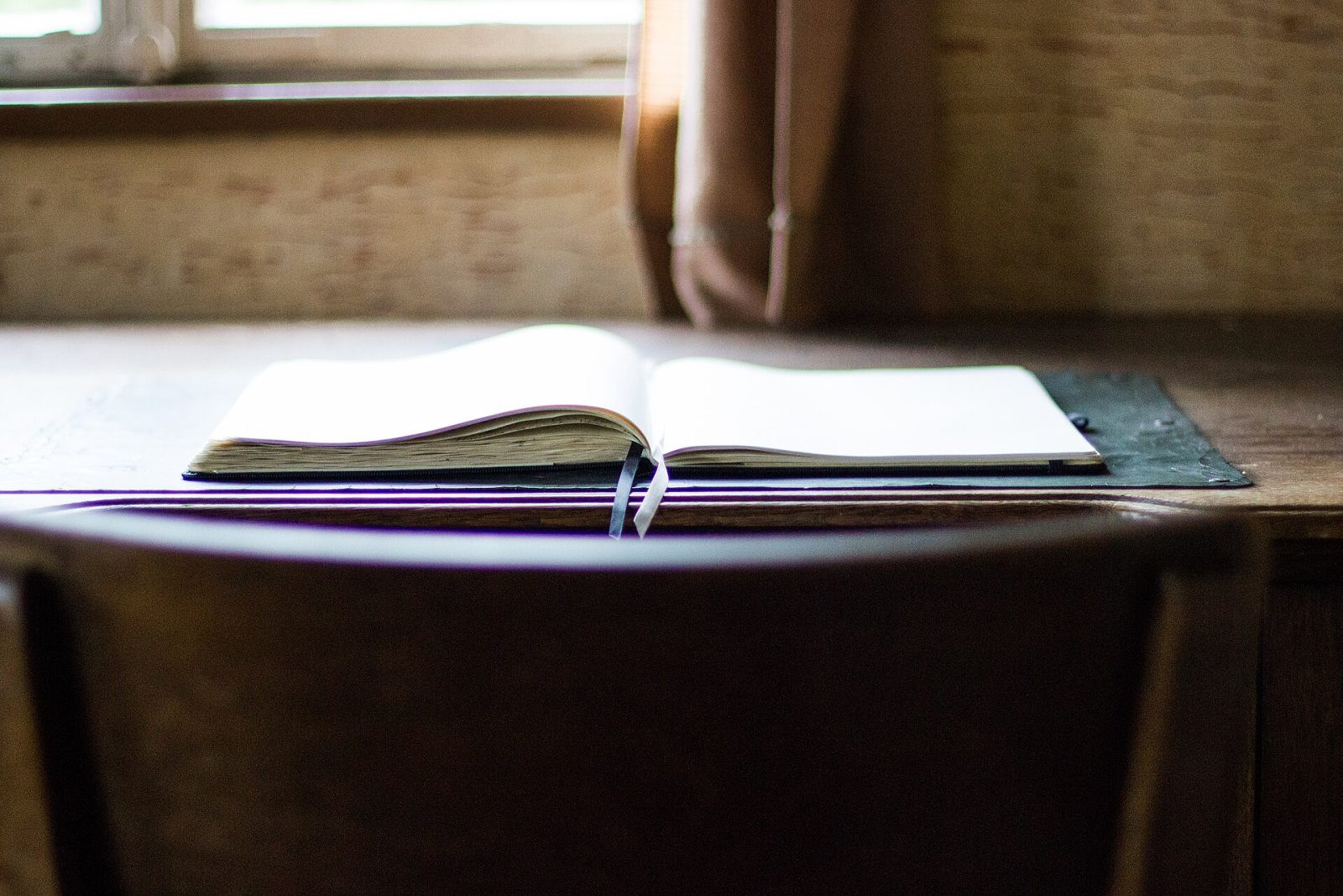 An open book on a wooden table by a window.