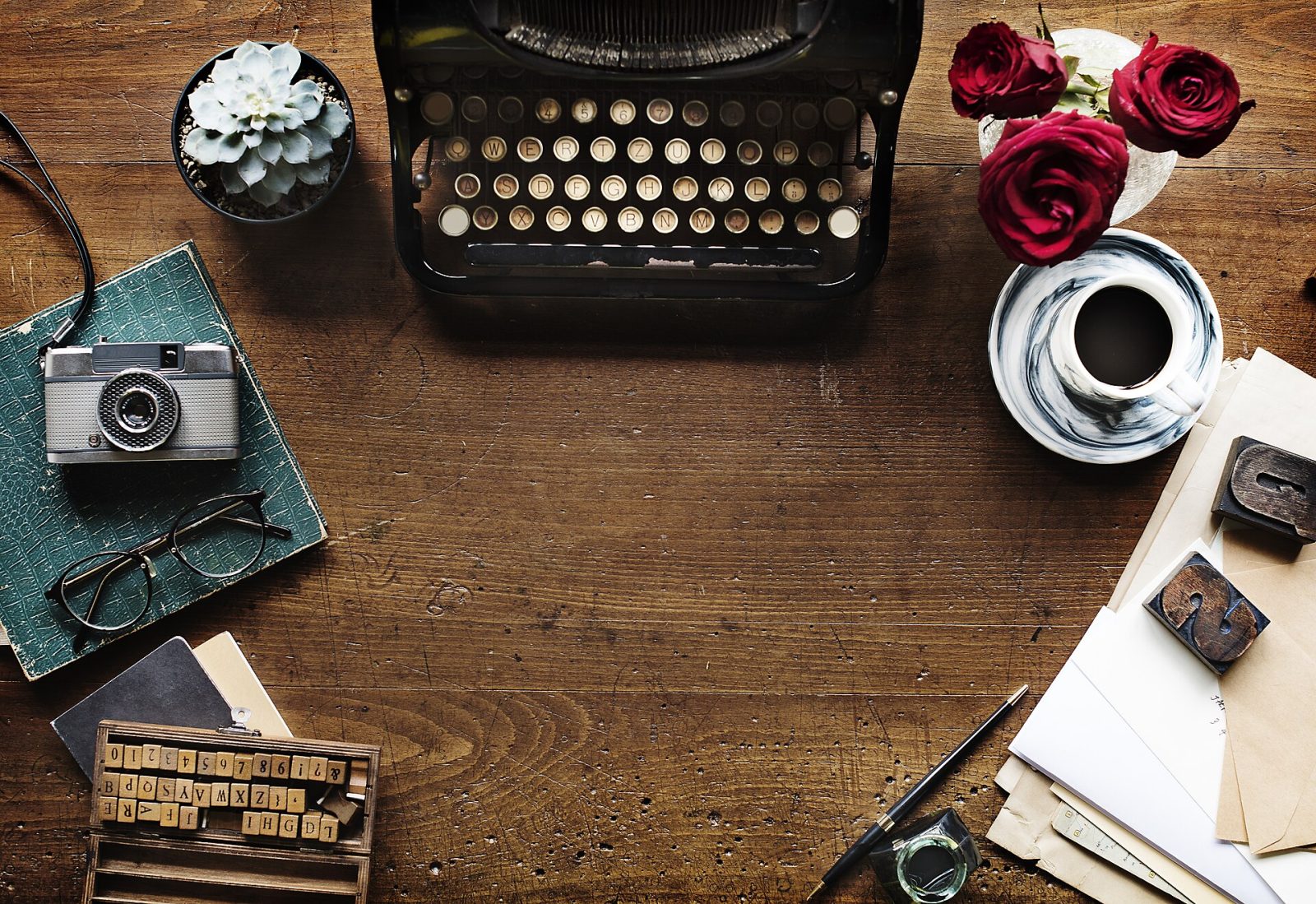 A flat-lay of a typewriter, cut flowers and a camera on a wooden desk.